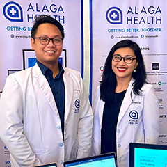 Dexter Galvan, CEO of Alaga Health with COO Dr. Via Roderos standing behind computer screens displaying the Alaga Health platform