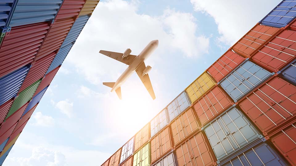 Cargo plane flying above stack of containers at container port