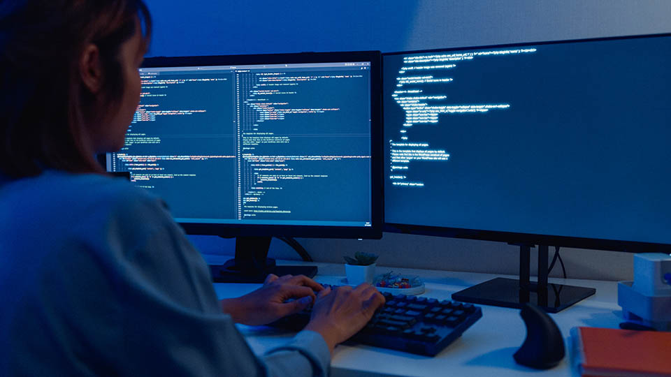 Young Asian woman software developers using computer to write code sitting at desk with multiple screens