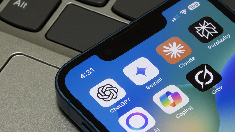 An iPhone with a blue case rests on a grey laptop keyboard, showing a home screen at 4:31 with a collection of leading AI chatbot applications, including OpenAI's ChatGPT, Google's Gemini, Anthropic's Claude, Perplexity AI, xAI's Grok, and Microsoft Copilot. The image highlights the rapid proliferation and mainstream adoption of generative AI assistants on mobile devices.