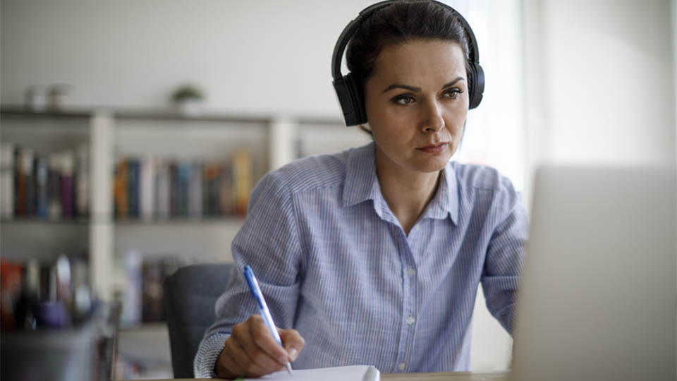 Woman watching a video on a laptop and taking notes