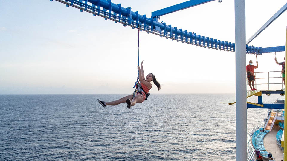Woman riding a zip line over the ocean on a cruise ship.