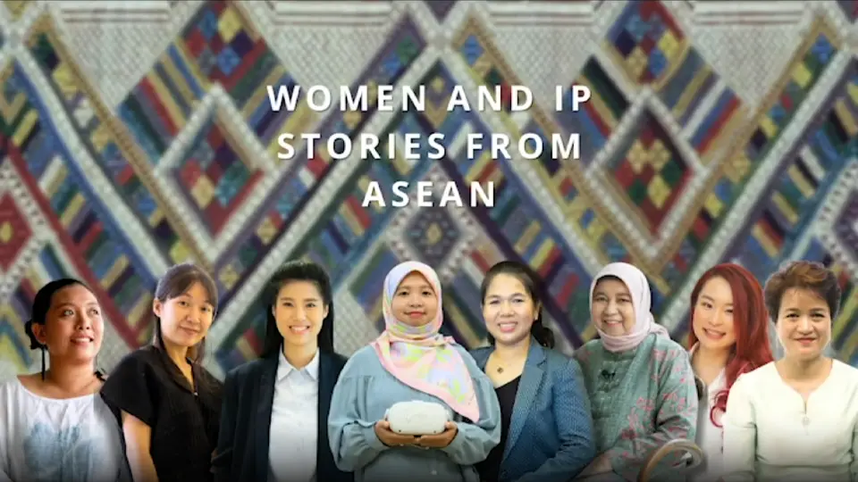 Seven diverse women stand before colorful Southeast Asian woven patterns