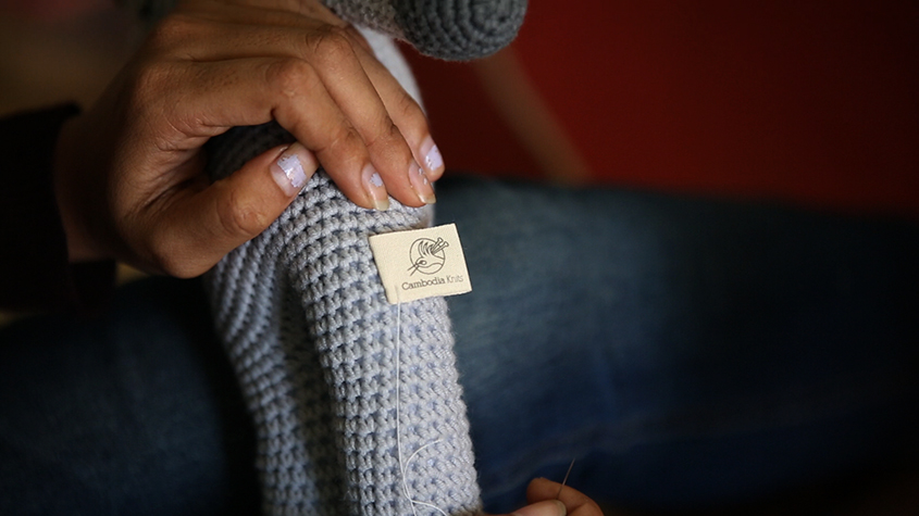 Hand sewing of a Cambodia Knits label on a knitted toy