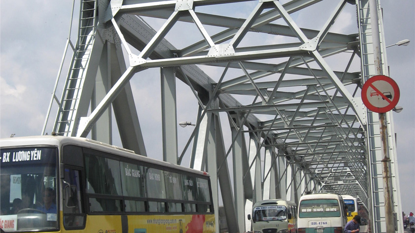 The Chuong Duong Bridge in Hanoi with grey paint from Prof. Nguyen with several colorful buses driving on the road underneath