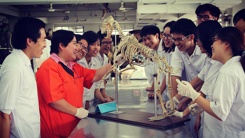 Assistant Professor Pawana Chuesiri surrounded by students in white blouses, studying a dog skeleton