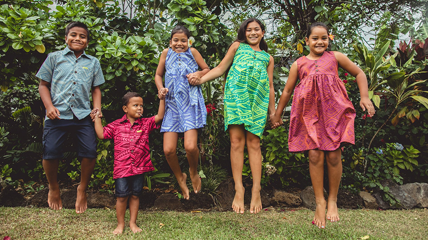 A group of three girls and two boys, most of them jumping in the air, wearing colorful EveniPacific shirts and dresses