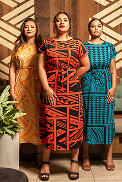 Three women standing and wearing colorful traditional Samoan design printed dresses