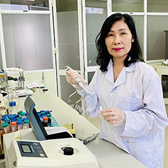 Hoang Phuong Hà, Deputy Head of the Environmental Bioremediation Laboratory at the VAST Institute of Biotechnology, sitting in her lab wearing a white lab coat, and transparent gloves, filling a test tube