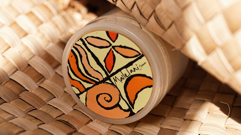 Mailelani lip balm with a lid decorated with the company’s logo in orange and yellow shades, showing a flower, waves, a shell, and the moon