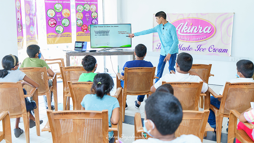 Nethila standing and pointing to a screen showing his course on how to run an ice cream shop to teenagers sitting on chairs