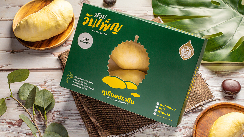 A peeled “Prachin Durian” on a wooden plate, next to the green packaging of the product.