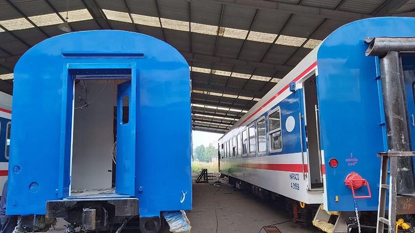 Two train cars freshly painted with blue, red, and white paint in a shed
