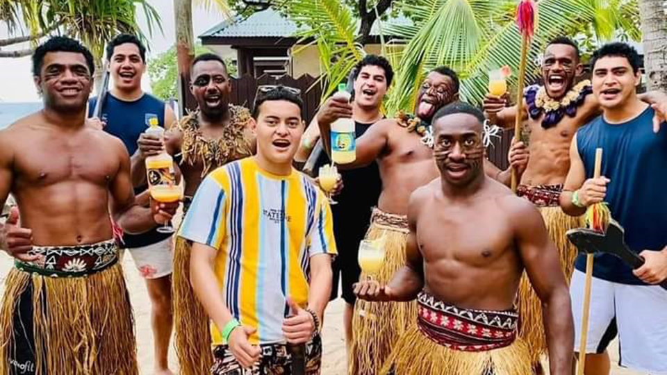 Fijian men wearing traditional Sulus are drinking cocktails containing CocoPine juices on the beach