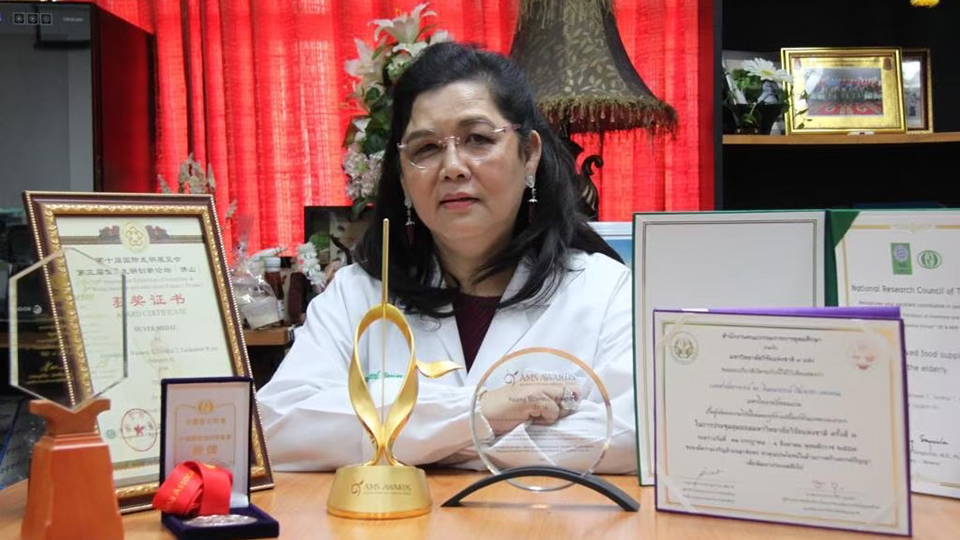 La doctora Jintanaporn Wattanathorn, cofundadora de JWF, sentada ante un escritorio en el que figuran varios galardones