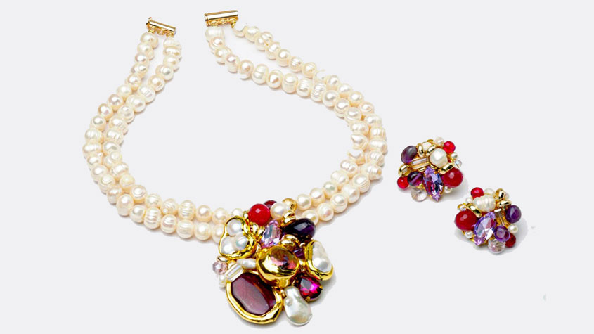Photo of a matching set of HABIBA pearl-encrusted necklace and earrings with shiny red, purple, violet and white gems from the Frida Collection.