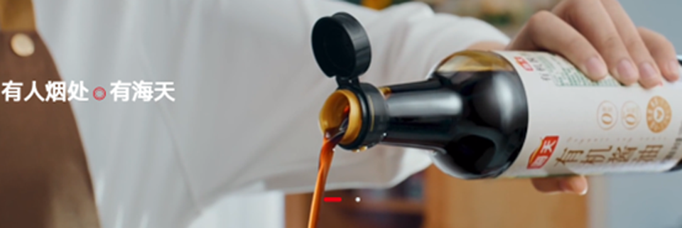Visual shows a close-up of a person in white clothes pouring soy sauce from a glass bottle into a dish.
