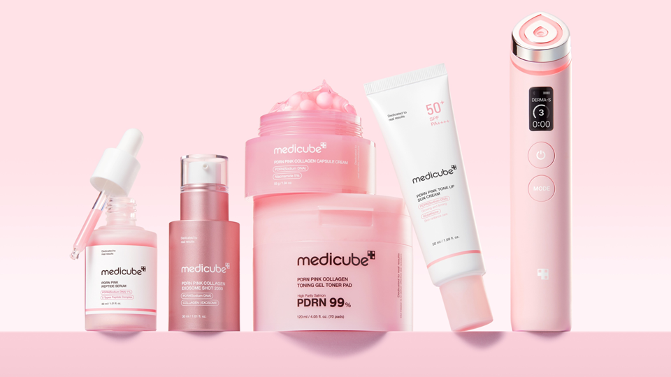 La foto muestra seis productos Medicube, entre ellos un suero, una crema solar, un gel tonificante y una crema de colágeno, así como el dispositivo portátil DERMA-S, todo ello sobre un fondo rosa.
