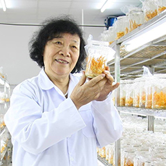 Dr. Chinh in a white lab coat, holding a glass jar with orange stringy mushrooms.
