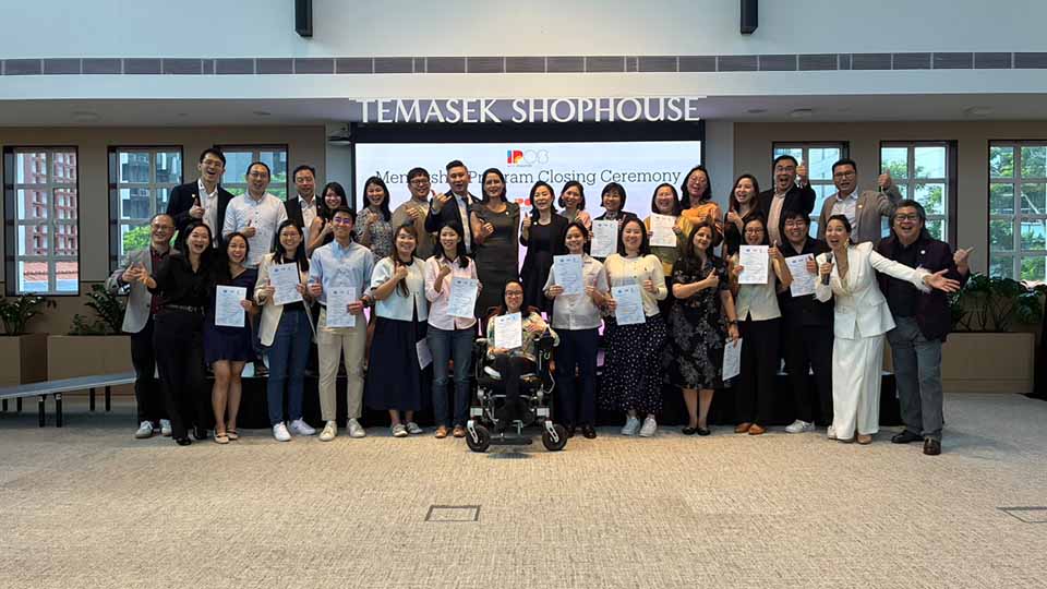 Large group of smiling participants holding certificates pose together at the Temasek Shophouse Mentorship Program Closing Ceremony, with one member seated in a motorized wheelchair at the front