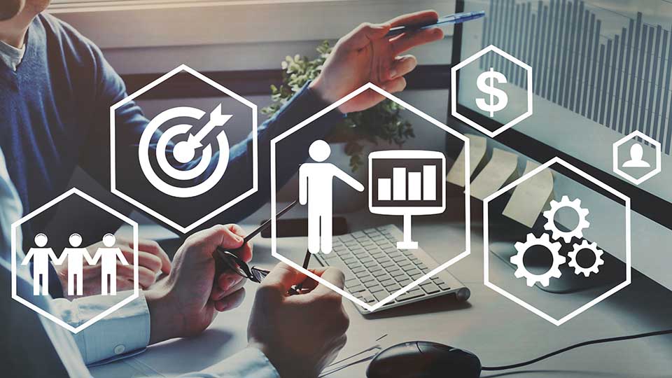 Business professionals at desk with overlaid hexagon icons representing target goals, team collaboration, data presentation, finance, settings, and user profile