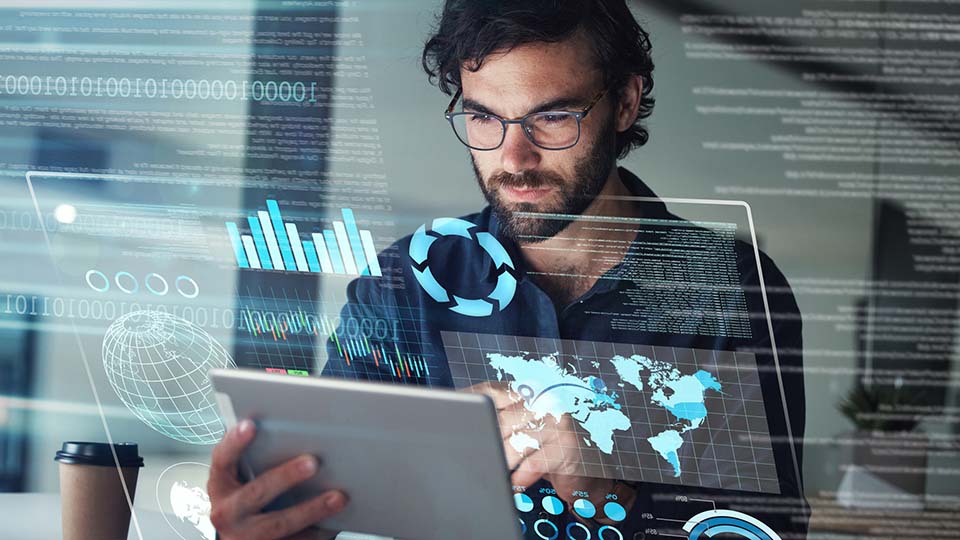 Bearded man wearing glasses analyzing data on a tablet, surrounded by holographic overlays of charts, world map, and binary code representing digital business analytics.