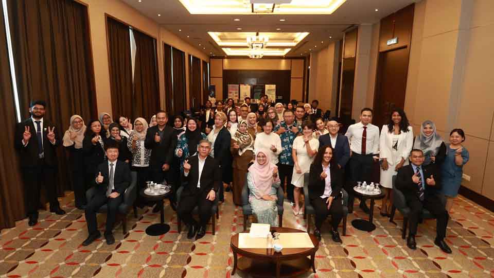 Large group of event participants smiling and giving thumbs-up for a group photo in a hotel function room