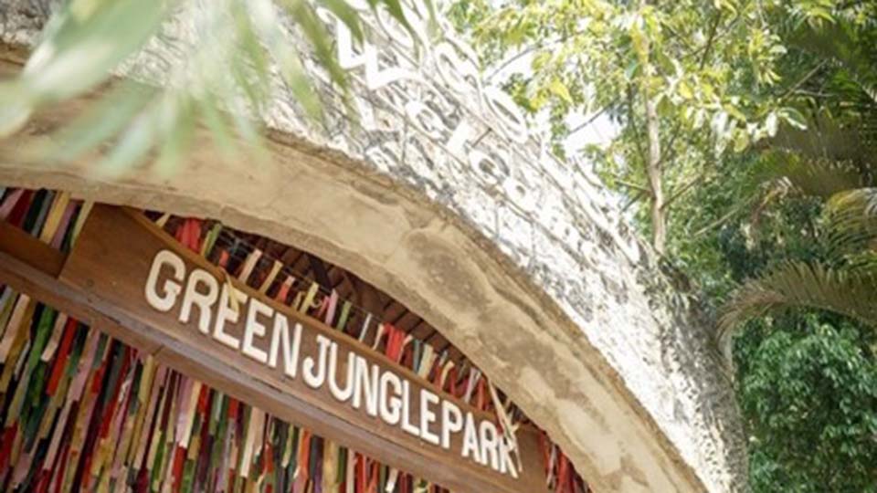 Stone arch entrance of Green Jungle Park decorated with colorful fabric strips, surrounded by trees