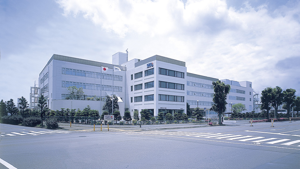 Exterior view of the Semiconductor Energy Laboratory (SEL) headquarters building with the Japanese flag and SEL logo visible on the facade