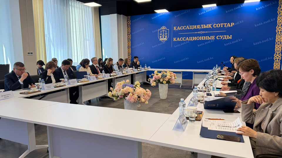 Delegates seated on both sides of conference tables during a formal bilateral meeting at the Cassation Courts of Kazakhstan, with floral centerpieces and the court's official blue branded backdrop bearing the website kass.sud.kz