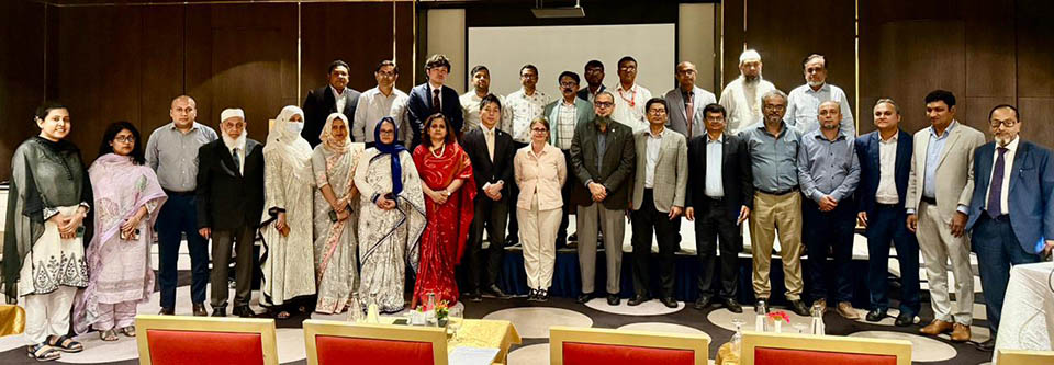 Mixed group of male and female professionals posing for a formal group photo at a conference or official meeting in a hotel banquet or conference room.