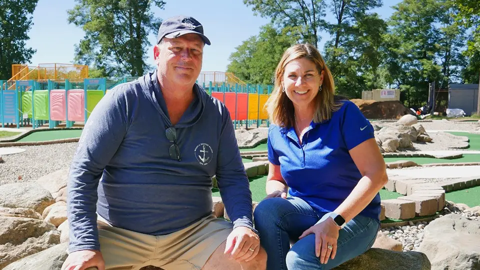 Jim and Michelle Liggett seated together beside a miniature golf course.