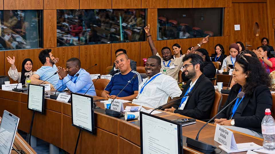 Delegates from multiple countries, including Jordan, India, and Indonesia, seated at conference tables with name placards, applauding and raising hands enthusiastically during a WIPO International Patent Drafting Training Program plenary session
