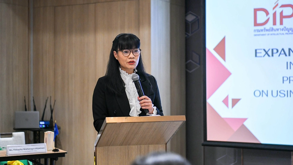 Woman speaking at a podium with a presentation screen visible beside her.