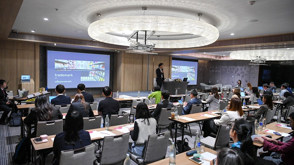 Man presenting on trademarks to seated attendees in a conference room, with two screens displaying the presentation.
