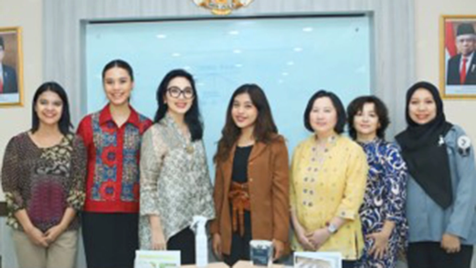 Group photo of seven women standing together in a formal office setting with the Indonesian national emblem and official portraits visible in the background