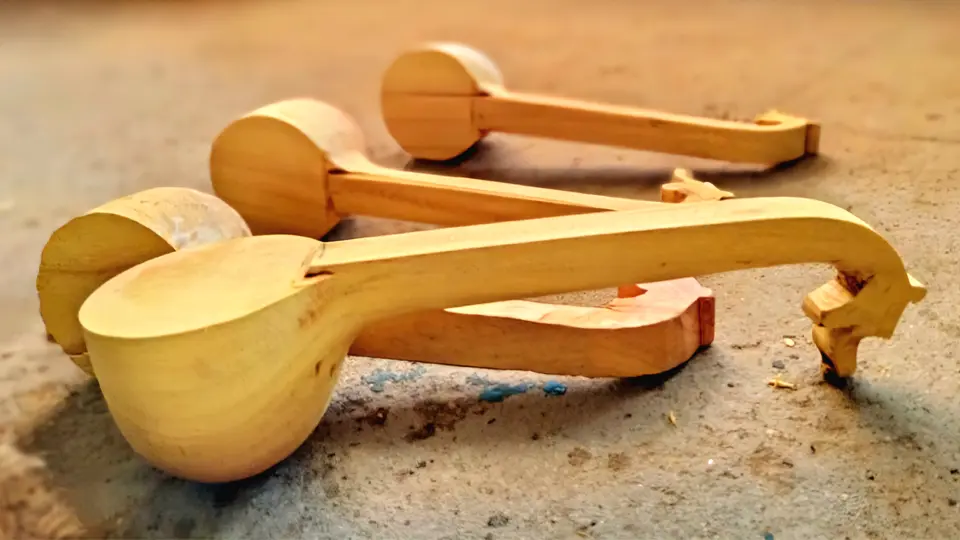 Miniaturas de vinas de Bobbili em madeira clara sem acabamento dispostas no chão, ainda numa fase inicial de fabricação.