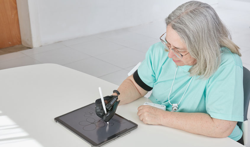 Photo of a woman drawing a picture of a flower on a tablet, using the Neomano glove to hold her pen.
