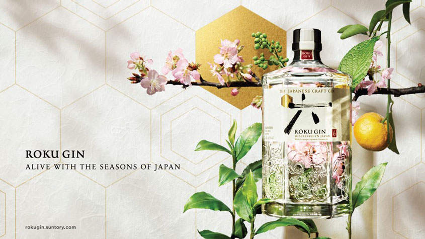A bottle of the gin “ROKU”, with a background of leaves , lemons and cherry tree flowers.