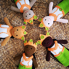 Five Aspara knitted dolls arranged on a braided dish, in a circle, with their heads touching and five different skin color tones
