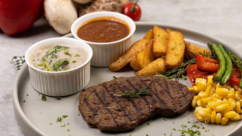 A plate with a beefless steak along with fries and vegetables