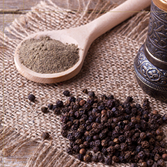 “Chanthabury Pepper” peppercorn on a mat next to a wooden spoon with ground pepper