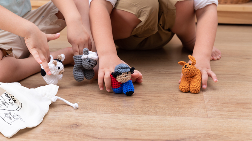Two children on the floor playing with four finger-knitted puppets representing farm animals