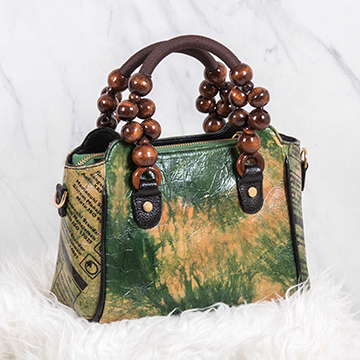 A shaded green HeySTARTIC handbag with markings from a recycled cement bag on its side, and a shoulder strap made out of fabric and wooden balls