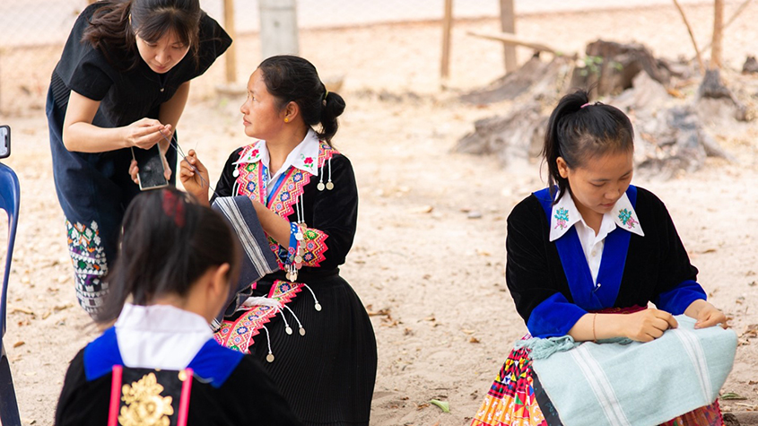 Photo of Douangmany looking over the works of her weavers
					