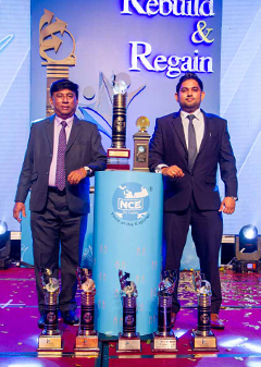 Vernon Abeyratne, JAPC Managing Director and his son Chathura Abeyratne, JAPC Director standing on a podium during the National Chamber of Export Award Ceremony 2021, with several awards at their feet