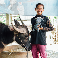 Chan Ny touching the head of a water buffalo and holding in the other hand “Bongo” the grey knitted water buffalo