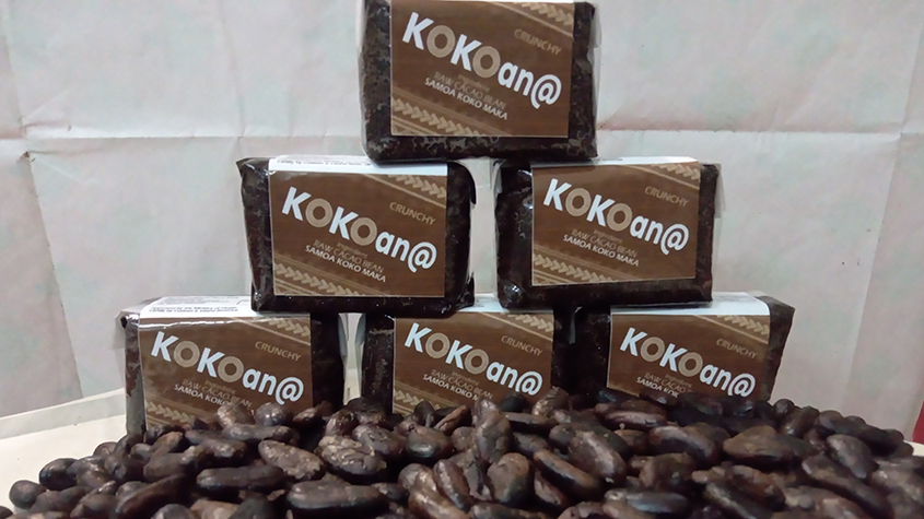 Several packets of KOKOan@ raw cacao paste stacked with at the foreground loose roasted cacao beans