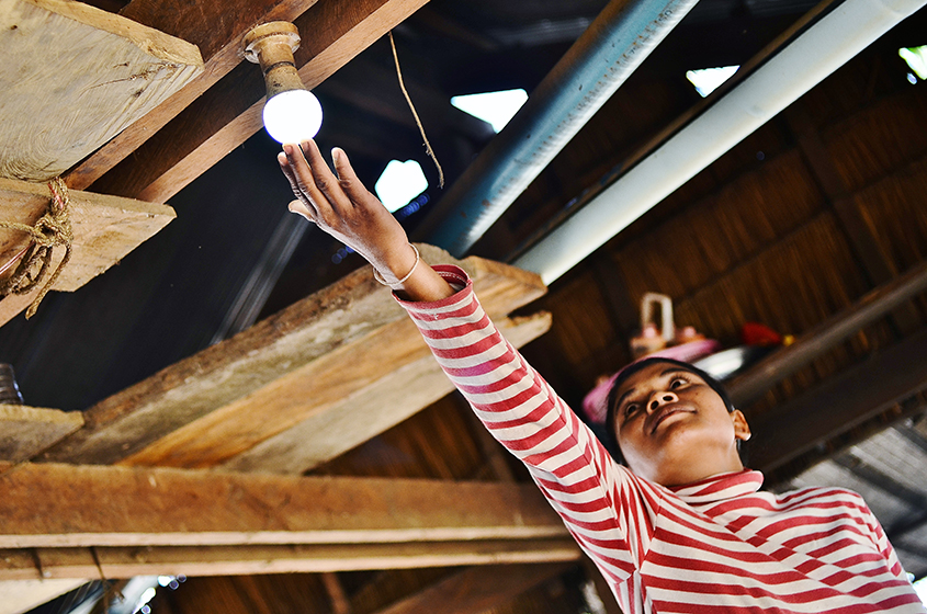 A young child in a rural house in Cambodia who is touching a lightbulb that is lightened up thanks to Okra Solar Mesh-Grids