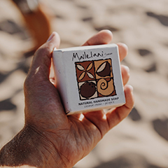 Man holding a Mailelani coconut soap in his hand in its original packaging featuring the company logo